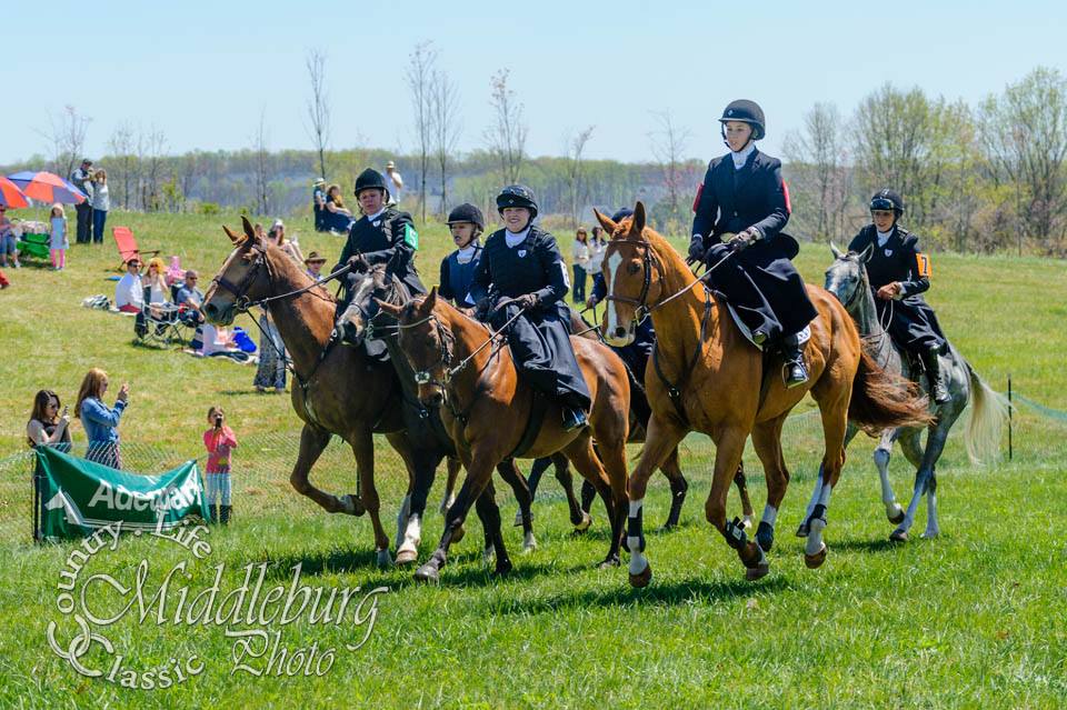 A group of people riding horses on a grassy field.