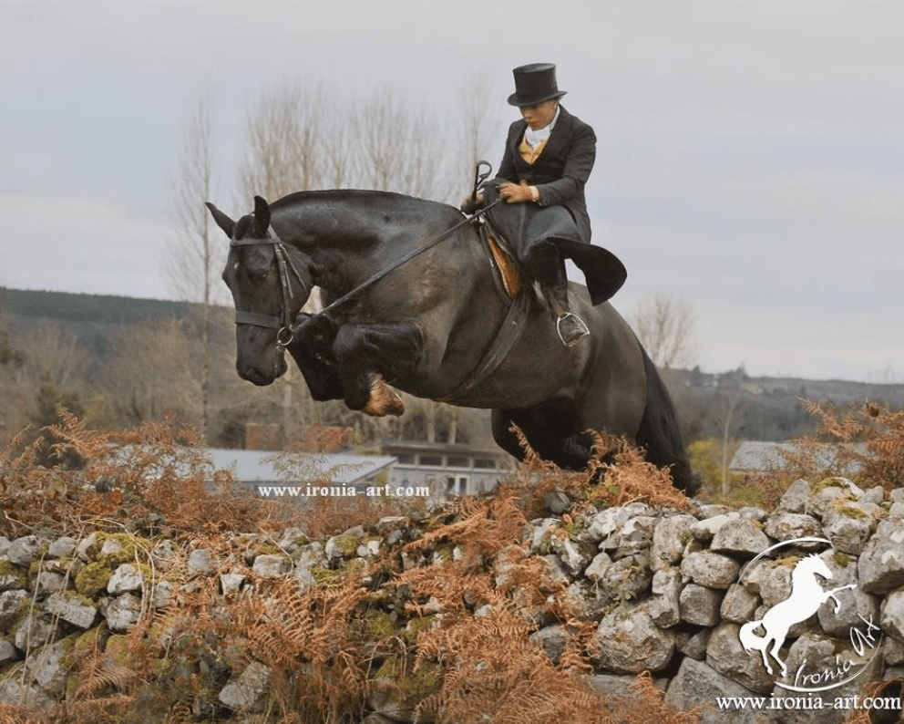 A man in a top hat riding a horse over a stone wall.