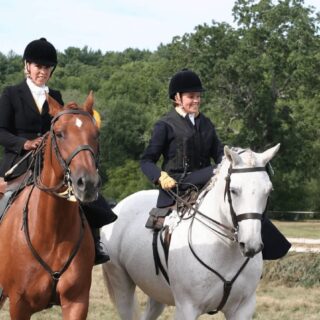 Two ladies riding two horses in open field