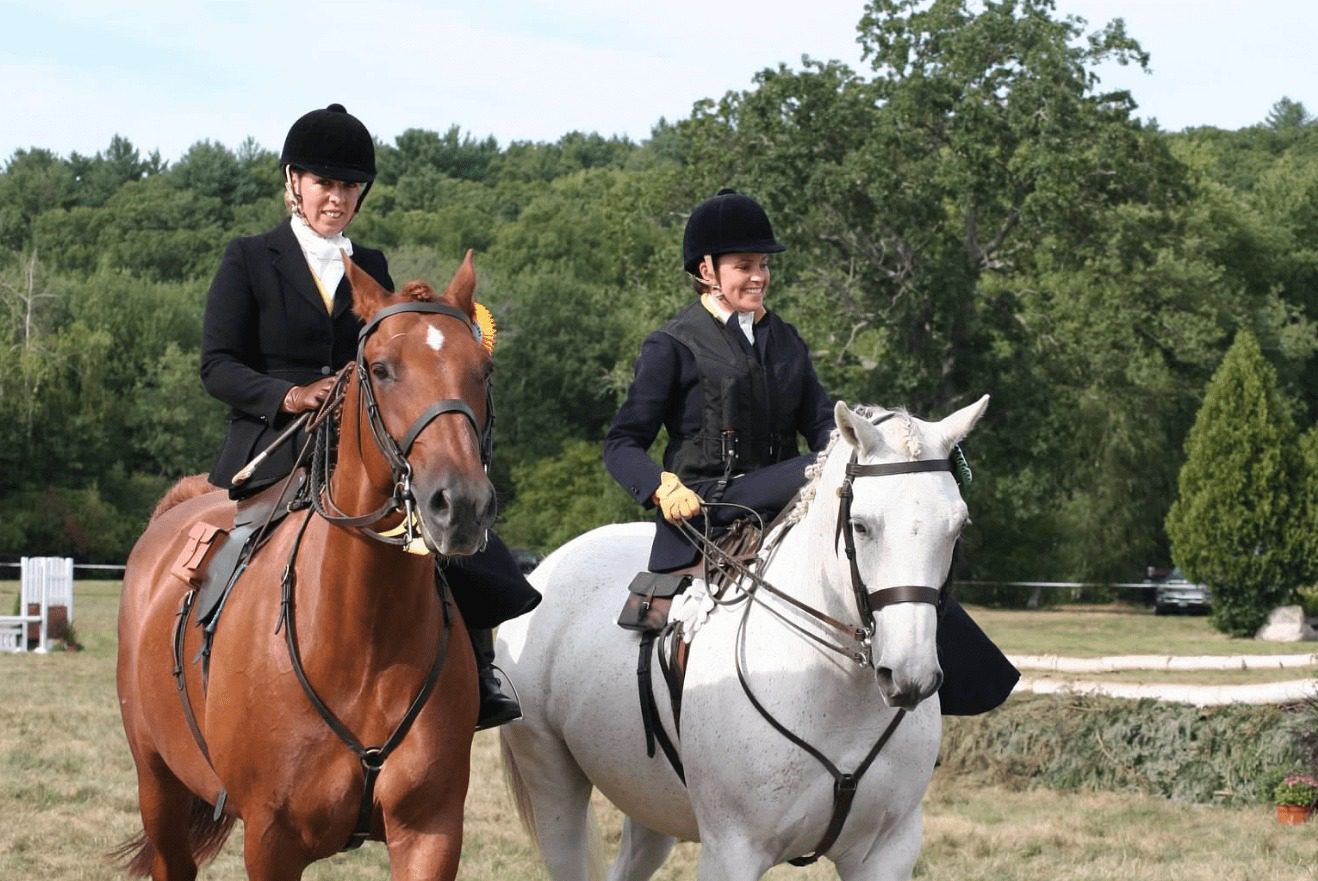 Two ladies riding two horses in open field